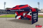 Namiot reklamowy z herbem klubu 3x6m – STADION – dwie ściany boczne z nadrukiem Namiot ekspresowy 3x6m z pełnym nadrukiem w barwach klubowych – dwie ściany boczne z herbem i nazwą klubu, rozstawiony przy bieżni lekkoatletycznej na stadionie
